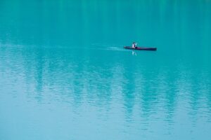 A lone canoeist paddles across a serene turquoise lake, embodying peace and solitude.