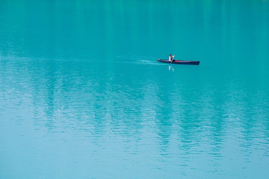 What It Means to Leave People Behind A lone canoeist paddles across a serene turquoise lake, embodying peace and solitude.
